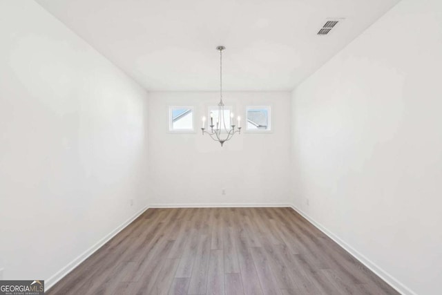 unfurnished dining area with a chandelier, visible vents, baseboards, and wood finished floors