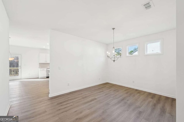 unfurnished dining area with visible vents, baseboards, a chandelier, and wood finished floors