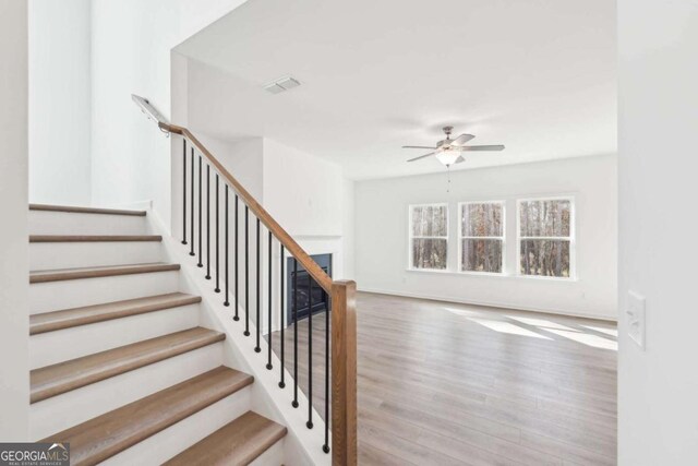 stairs featuring wood finished floors, a ceiling fan, and visible vents