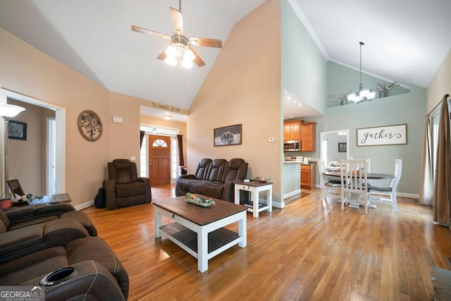 living area with light wood-type flooring, ceiling fan with notable chandelier, high vaulted ceiling, and baseboards