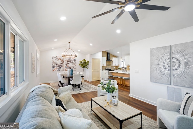 living room featuring ceiling fan with notable chandelier, dark wood finished floors, visible vents, lofted ceiling, and baseboards