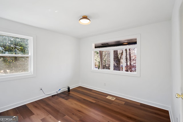 spare room with visible vents, baseboards, and dark wood finished floors