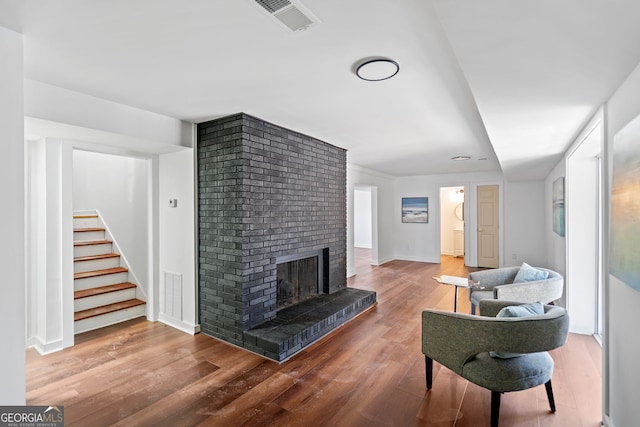 living room with wood finished floors, a brick fireplace, visible vents, and stairway