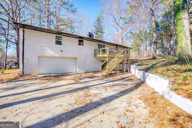 back of property with a wooden deck, stairway, brick siding, a garage, and driveway