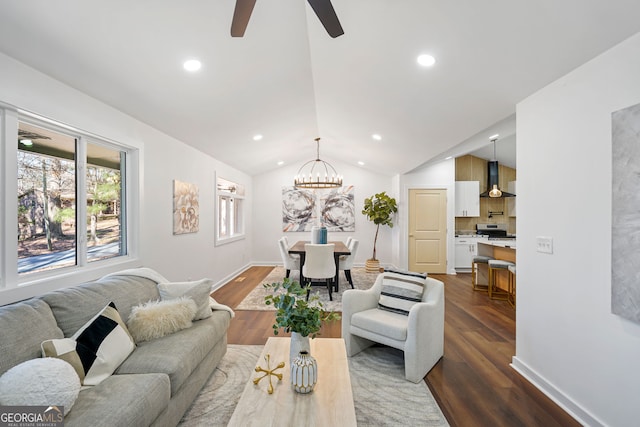 living area with dark wood-type flooring, ceiling fan with notable chandelier, baseboards, and vaulted ceiling