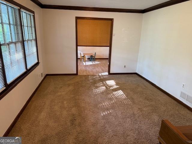 carpeted spare room featuring visible vents, baseboards, and crown molding