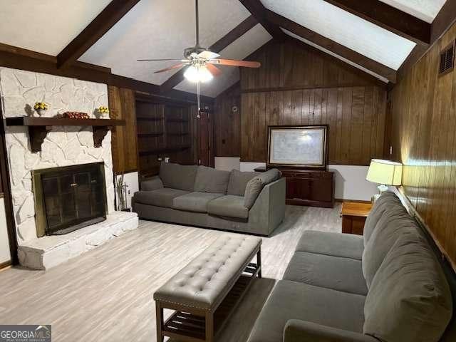 living room featuring light wood finished floors, wooden walls, ceiling fan, and vaulted ceiling with beams