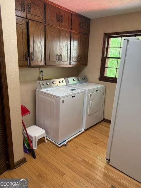 laundry area featuring light wood finished floors, independent washer and dryer, and cabinet space