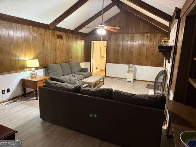 living area with visible vents, ceiling fan, wooden walls, light wood finished floors, and vaulted ceiling with beams