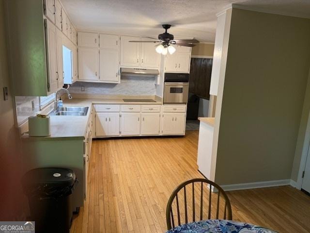 kitchen with light countertops, under cabinet range hood, oven, light wood finished floors, and a sink