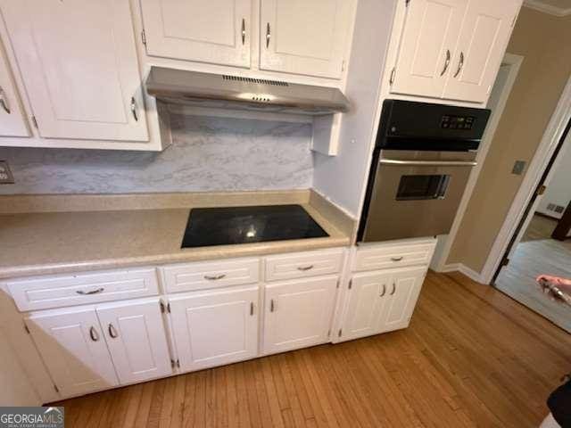 kitchen featuring white cabinets, under cabinet range hood, black electric stovetop, and stainless steel oven