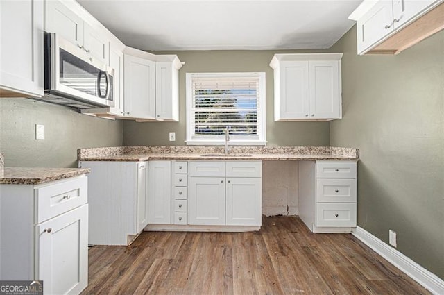 kitchen with a sink, dark wood finished floors, stainless steel microwave, white cabinetry, and light stone countertops