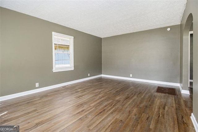 empty room with arched walkways, a textured ceiling, baseboards, and wood finished floors
