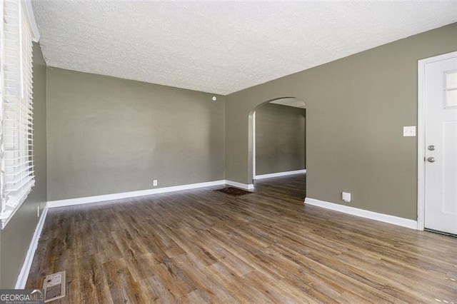 interior space featuring arched walkways, a textured ceiling, visible vents, wood finished floors, and baseboards