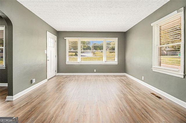 empty room featuring arched walkways, wood finished floors, baseboards, and visible vents
