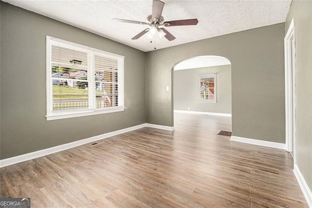 spare room featuring arched walkways, wood finished floors, a ceiling fan, and a healthy amount of sunlight