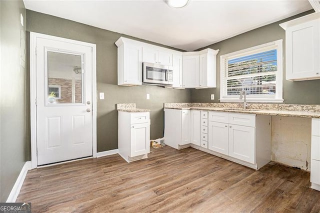 kitchen with stainless steel microwave, light stone counters, white cabinets, a sink, and wood finished floors