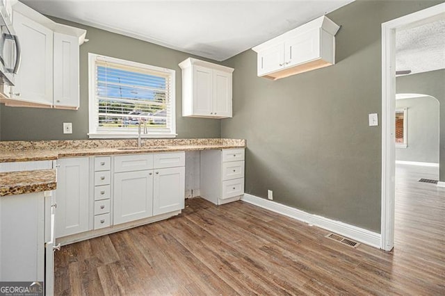 kitchen featuring visible vents, baseboards, a sink, and wood finished floors