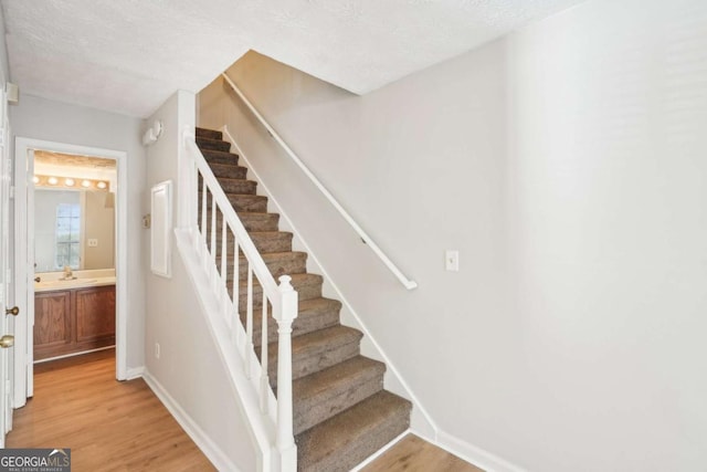 stairway featuring baseboards, a textured ceiling, and wood finished floors