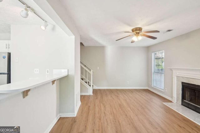 unfurnished living room featuring light wood-style floors, ceiling fan, a fireplace, rail lighting, and baseboards