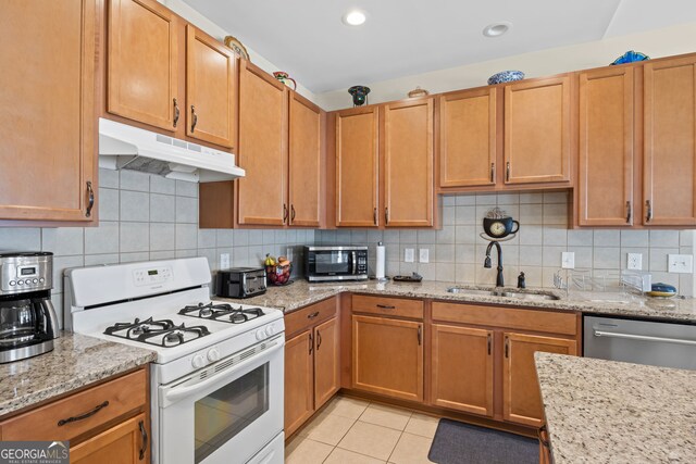 kitchen featuring appliances with stainless steel finishes, light tile patterned floors, under cabinet range hood, decorative backsplash, and a sink