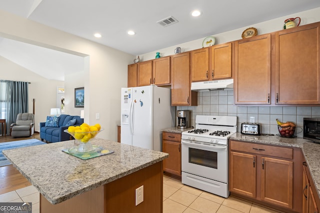 kitchen with white appliances, light tile patterned floors, a kitchen island, under cabinet range hood, and visible vents