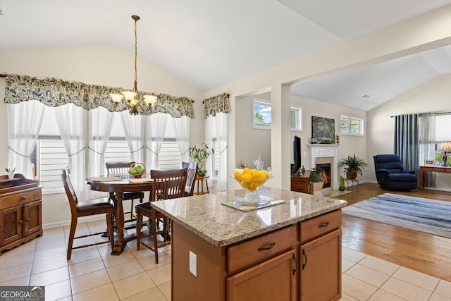 kitchen with a chandelier, vaulted ceiling, a lit fireplace, a kitchen island, and light tile patterned flooring