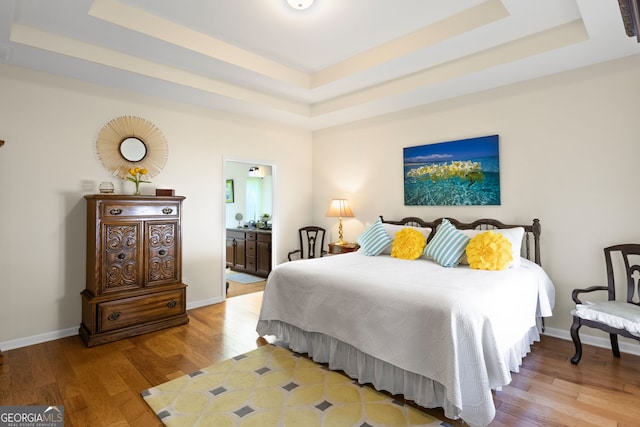 bedroom featuring ensuite bath, a tray ceiling, baseboards, and wood finished floors