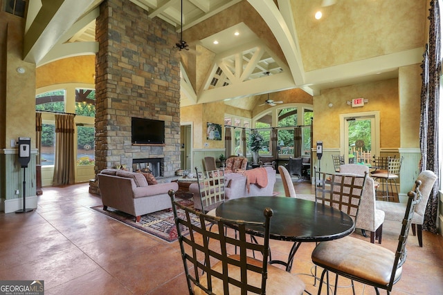 dining space with a towering ceiling, an outdoor stone fireplace, visible vents, beam ceiling, and ceiling fan