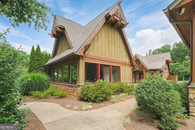 exterior space with board and batten siding, stone siding, a sunroom, and roof with shingles