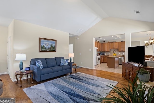 living area featuring visible vents, light wood finished floors, a notable chandelier, and lofted ceiling