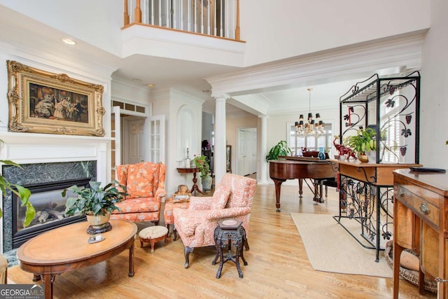 living room with an inviting chandelier, ornamental molding, decorative columns, light wood finished floors, and a glass covered fireplace