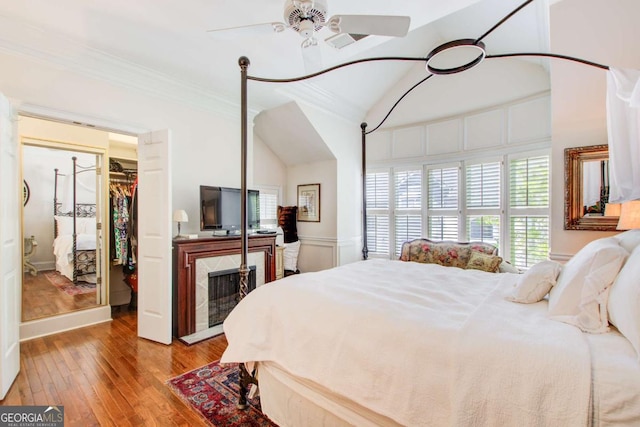 bedroom with ornamental molding, a walk in closet, lofted ceiling, a high end fireplace, and hardwood / wood-style flooring