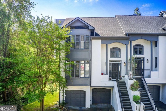 view of property featuring stairway, a shingled roof, stucco siding, and an attached garage
