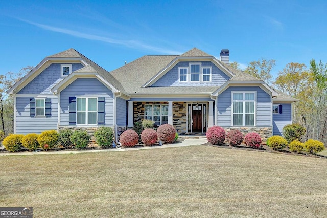 craftsman-style home featuring a front lawn, a shingled roof, stone siding, and a chimney