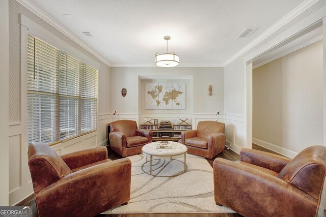living area featuring a decorative wall, visible vents, crown molding, and wood finished floors