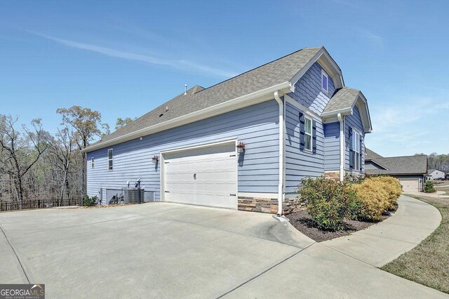 view of property exterior with central AC unit, stone siding, a garage, fence, and concrete driveway