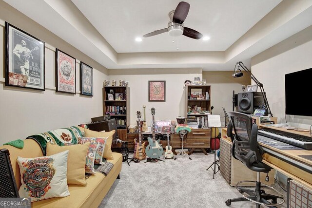 carpeted office space with a tray ceiling and ceiling fan