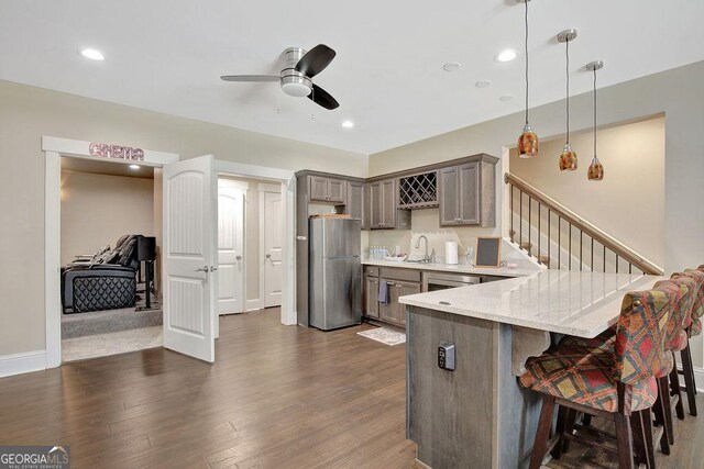kitchen featuring a kitchen breakfast bar, a peninsula, freestanding refrigerator, ceiling fan, and a sink