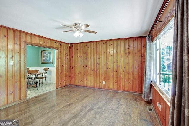 unfurnished room with baseboards, wood walls, visible vents, ceiling fan, and wood finished floors