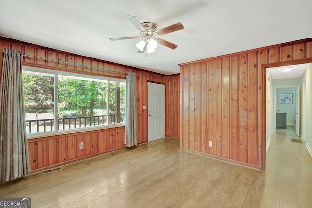 spare room featuring visible vents, baseboards, a ceiling fan, wooden walls, and wood finished floors