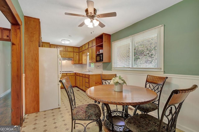 dining area with a ceiling fan, a wainscoted wall, and light floors