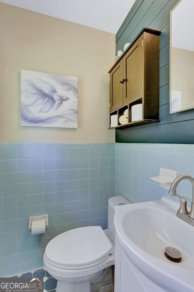 bathroom with toilet, a sink, and tile walls