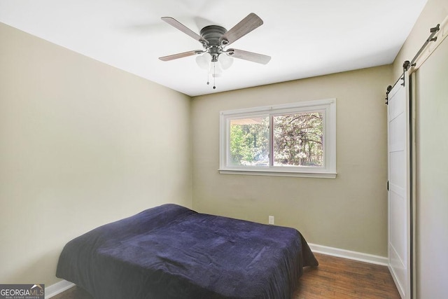bedroom featuring a barn door, ceiling fan, baseboards, and wood finished floors