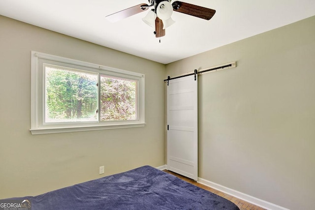 bedroom with baseboards, a ceiling fan, a barn door, and wood finished floors