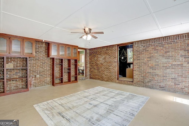 unfurnished living room featuring brick wall, finished concrete floors, and a ceiling fan