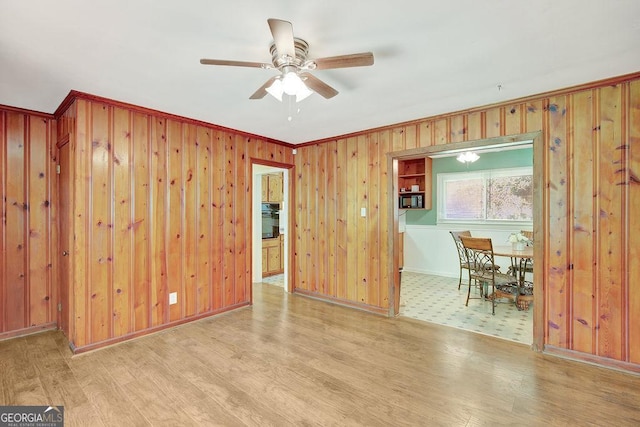 spare room with crown molding, ceiling fan, wood finished floors, wooden walls, and baseboards