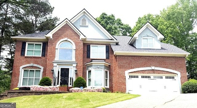 colonial home with driveway, roof with shingles, a front yard, and brick siding