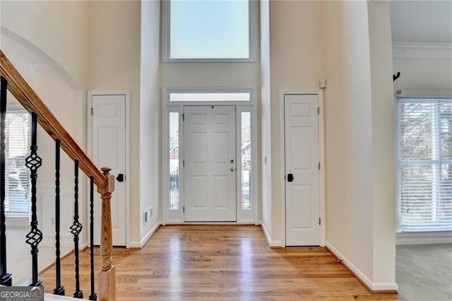foyer with a towering ceiling, light wood finished floors, stairway, and a wealth of natural light