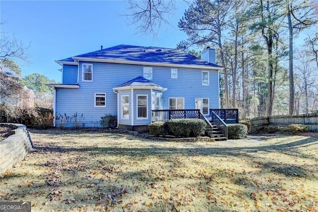 rear view of house with a deck, a chimney, a fenced backyard, and a lawn